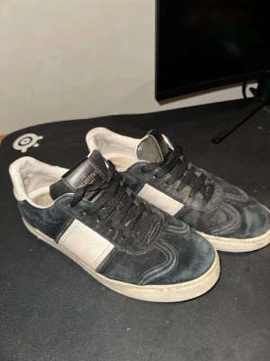 Valentino flycrew - Säljer ett par Valentino Garavani sneakers i svart mocka med vita detaljer och svart snörning. Skorna har en klassisk låg siluett och rund tå. Sulan har ett unikt mönster undertill och märkeslogga på plösen. Perfekta för dig som gillar exklusiva streetwear-vibbar.