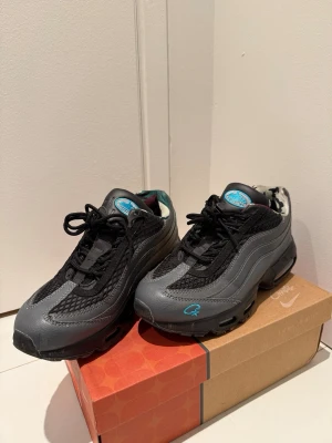 Nike Air Max 95  - Nike Air Max 95  i grått och svart med turkosa detaljer. Ovandel i mesh och skinn, med synlig Air Max-dämpning i sulan. Insidan har ett unikt camouflagemönster och snörning framtill. Snygg och chunky siluett med rund tå och platt sula. Använd fåtal gånger. Stl 42 men sitter som 41. Det finns en lite defekt när du kunde snöret har gått sönder men går att fixa.
