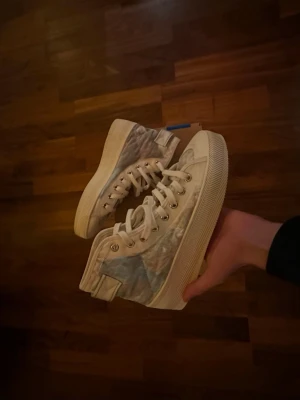 Adidas höga sneakers med marmorprint - Säljer ett par höga sneakers från Adidas med vit bas och marmorliknande mönster i grått, blått och rosa på sidorna. Skorna har snörning, rund tå och platt sula. Adidas-logga på plösen och klassisk retrostil. Perfekt för dig som gillar unika detaljer och streetwear.
