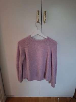 Ljusrosa stickad tröja från H&M - Mysig ljuslila stickad tröja från H&M med rund hals och ribbade muddar vid ärmslut och nederkant. Perfekt för kyliga dagar och enkel att matcha med jeans eller kjol. Tröjan har en klassisk passform och är långärmad.