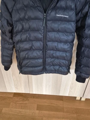 Svart Peak Performance dunjacka - Svart dunjacka från Peak Performance stl 170. Finns en liten reva men det finns duntejp som jag skickar med. 750 kr