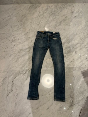 Dondup George jeans, storlek 28 - Säljer ett par Dondup George jeans  i  storlek 28. Modellen är slim fit med raka ben. Jeansen har snygga slitningar och detaljer som bruna sömmar och läderpatch bak i midjan. Perfekt för dig som gillar en tidlös och cool look. Längd 101cm