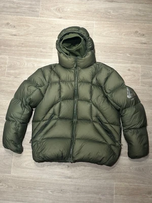 Palace balaclava puffer - Säljer en fet mörkgrön dunjacka från Palace med huva och två sidofickor med dragkedja. Jackan har loggan på armen samt huvan. Perfekt för kalla dagar 🥶🙏. Inga märken alls förutom det lilla av texten som lossnat i jackan och på balaclavan som man ser på bilderna. Annars knappt använd alls. Den är från FW 22.