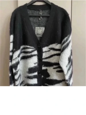 Svartvit zebra-kofta från GCDS - Säljer en fluffig och oversized kofta från GCDS med svartvitt zebramönster. Koftan har v-ringning, knappar framtill och lång ärm. Materialet är stickat och känns mjukt mot huden. Perfekt för dig som gillar statement-plagg och djurmönster.