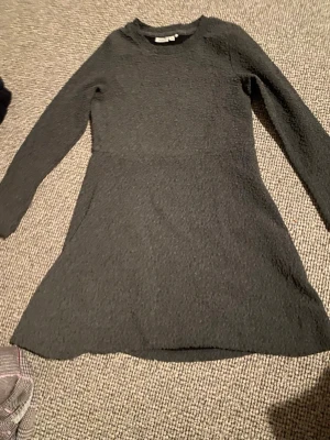 Mörkgrå långärmad klänning Name It - Säljer en mörkgrå klänning från Name It i storlek 134. Klänningen har lång ärm, rund hals och ett diskret strukturmönster i tyget som ger en cool känsla. Modellen är lätt utsvängd nedtill och passar perfekt för dig som gillar enkel och stilren design.