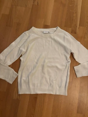 Vit stickad tröja från Vila - Klassisk vit stickad tröja från Vila i storlek S. Tröjan har rund halsringning, ribbade muddar vid ärmslut och nederkant samt lång ärm. Den är använd ett fåtal gånger.