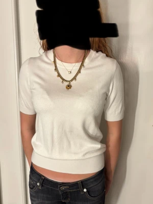 Vit kortärmad topp  - Säljer en stilren vit topp med korta ärmar och rund hals. Toppen och har en mjuk, ribbad kant nedtill. Perfekt att matcha med jeans eller kjol för en enkel och fräsch look.