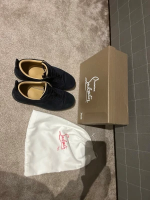 Mörkblå sneakers från Christian Louboutin - Säljer ett par mörkblå sneakers från Christian Louboutin i storlek 43. Skorna har en snygg röd sula med Louboutin-logga, ovandel i mocka och innersula i beige skinn. Klassisk rund tå och snörning framtill. Kommer med originalkartong och dustbag. Äkta kvitto finns ändå defekten: heeldrag