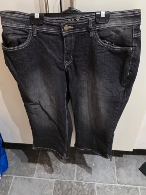 Svarta jeans från John Baner, stl 44 3/4 längd  - Säljer ett par svarta jeans från John Baner med kontrasterande vita sömmar och klassisk femficksdesign. Jeansen har raka ben och normal passform, tillverkade i jeansmaterial. Perfekta för dig som gillar en enkel och stilren look.