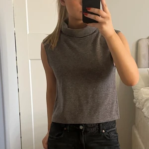 Grå ärmlös polotopp - Säljer en stilren grå polotopp i mjukt material. Toppen är ärmlös och har en hög krage. Passformen är normal.