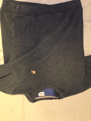 Mörkgrå tröja från Burberry  - Snygg mörkgrå tröja från Burberry i storlek M för att den är i barnstorlek .Tröjan har ett litet guldfärgat Burberry-logomärke broderat på bröstet och rund halsringning med blått tyg på insidan. Perfekt för dig som gillar klassisk stil med en lyxig touch.