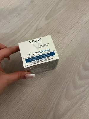 Vichy Liftactiv Supreme ansiktskräm - Vichy Liftactiv Supreme är en ansiktskräm i en vit och blå förpackning på 50 ml. Krämen är framtagen för att motverka rynkor och ge huden mer spänst. Passar normal och kombinerad hud. Förpackningen är av kartong och har tydliga produktbeskrivningar på framsidan.