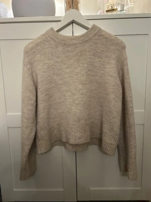 Beige stickad tröja från Gina Tricot - Mysig beige stickad tröja från Gina Tricot i storlek 146/152. Tröjan har ribbade muddar vid ärmslut, nederkant och halsringning. Enkel och stilren design som passar till det mesta.