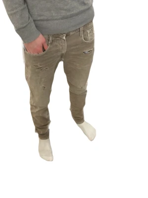 Bruna Replay jeans med slitningar - Säljer ett par bruna replay jeans med snygga slitningar och detaljer på framsidan. Byxorna har klassisk femficksdesign och smal passform som sitter tajt längs benen. Materialet är jeans och färgen är en neutral brun/beige som passar till det mesta. W30 L31