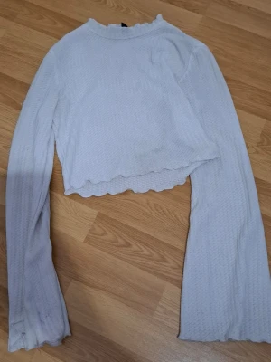 croppad tröja - Säljer en vit croppad långärmad topp med vågig kant nertill och vid ärmslut. Toppen har en ribbad struktur och är tillverkad i ett mjukt, stretchigt material som känns bekvämt mot huden. Perfekt till jeans eller kjol för en enkel men söt look.