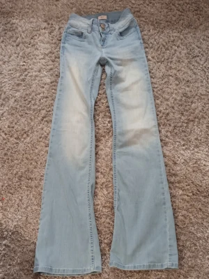 Bootcut ljusblå jeans från Nelly - Säljer ett par ljusblå bootcut jeans från Nelly med snygga detaljer som dubbla knappar och rosa sömmar. De är i fint skick, men som man kan se på 2 av bilderna i slutet så är det ett pyttelitet hål i ena bakfickan och ett längst ner vid ena benet, men det är inget som man tänker på.