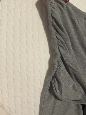 Grå omlott tubtopp från H&M Divided - Säljer en grå tubtopp från H&M Divided i omlottmodell med snygga rynkade detaljer på sidan. Toppen är ärmlös och har en mjuk, stretchig känsla tack vare bomullsmaterialet. Perfekt att styla med jeans eller kjol för en chill look.