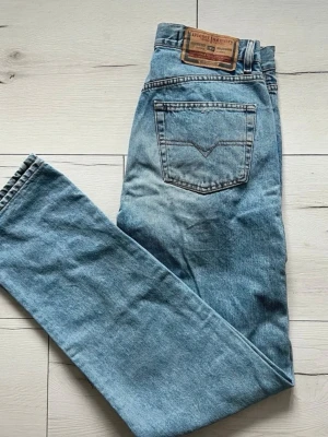 Blå straight jeans från Diesel Industry - Snygga ljusblå jeans från Diesel Industry med klassisk femficksdesign och raka ben. Jeansen har en tydlig Diesel Industry-patch baktill och detaljerade sömmar. Materialet är slitstark denim i bomull och passformen är normal med straight snitt.