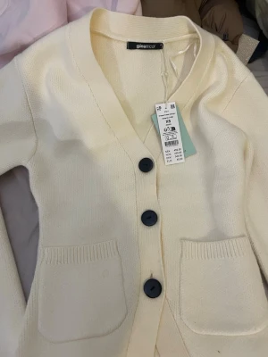 Beige kofta från Gina Tricot - Säljer en beige kofta från Gina Tricot i storlek XS. Koftan har v-ringning, tre stora knappar helt oanvänd