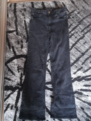Svarta bootcut jeans med hög midja - Snygga svarta jeans med bootcut-snitt och hög midja. Klassisk femficksmodell med knapp och dragkedja framtill. Jeansen har en mörk tvätt och är tillverkade i jeansmaterial. Perfekta för dig som gillar en retro vibe och vill ha lite extra vidd vid bensluten.