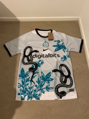 Nike Inter Milan fotbollströja  - Säljer en Nike Inter Milan fotbollströja i storlek XL med Dri-Fit ADV-teknologi. Tröjan är vit med svarta och turkosa detaljer, har ett grafiskt mönster med ormar och blommor samt svart krage och ärmslut. Perfekt för dig som gillar unik design och fotboll.