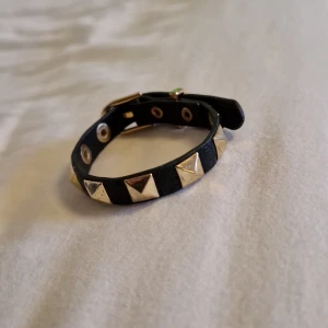 Svart armband med nitar och spänne - Coolt svart armband med guldiga pyramidformade nitar och justerbart spänne. Armbandet har en edgy vibe och passar perfekt för dig som gillar detaljer som sticker ut. Aldrig använd. Säljer för den var för stor för mig.