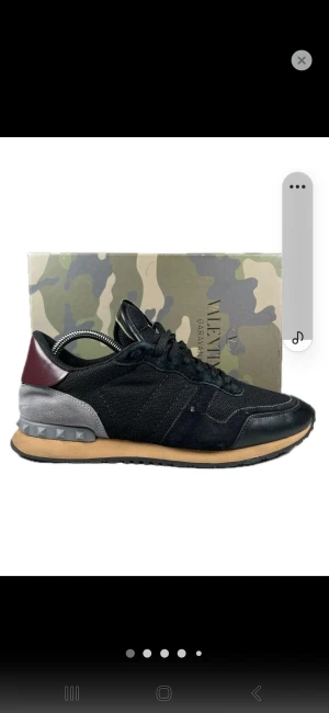 Valentino Garavani Rockrunner sneakers - Svarta Valentino Garavani Rockrunner sneakers med detaljer i vinrött och grått. Snygg mix av mocka, mesh och skinn, samt ikoniska nitar på hälen. Platt sula i beige och svart, rund tå och snörning framtill. Perfekt för dig som vill ha en lyxig streetstil.