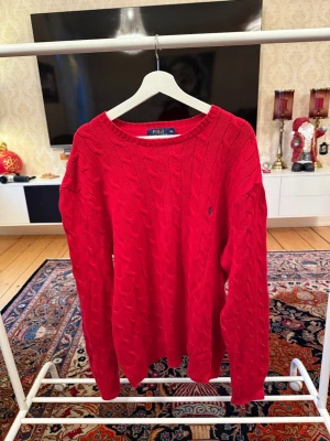 Polo Ralph lauren stickad tröja - Riktigt snygg röd kabelstickad tröja från Polo Ralph Lauren. Klassisk rund halsringning, diskret broderad logga på bröstet och ribbade muddar. Perfekt för dig som gillar en tidlös och preppy stil. Vid minsta funderingar så är det bara att höra av sig mvh CH 