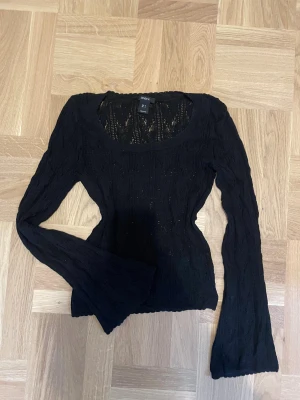 Svart stickad spets topp från Lindex - Svart stickad topp från Lindex med långärmade trumpetärmar och genombrutet mönster. Modellen är slim och har en rundad halsringning. Använd ändats en gång