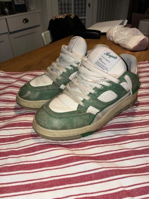 Axel Arigato gröna och vita sneakers - Säljer ett par feta sneakers från Axel Arigato i vitt och grönt. Skorna har en chunky beige sula, gröna mockadetaljer och vita meshpaneler. Klassisk snörning och låg profil. Perfekta för dig som vill sticka ut med stilrena men ändå unika sneakers. Tagit väl hand om dom. Ser lite slitna ut men det är lite av stilen på dom skorna.  Karton och påse ingår