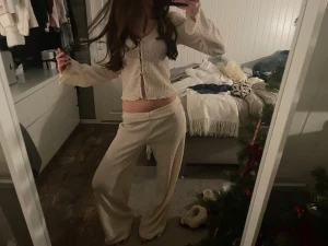 Beiget set med textur - Säljer en beige croppad kofta med långärmade, lätt utsvängda ärmar och snygga guldfärgade knappar framtill. Materialet är ribbat och har en skön, stretchig känsla. Perfekt för dig som gillar trendiga och bekväma plagg med lite extra attityd. Säljer båda delarna för 300! Byxorna är lite slitna längst ner vid hälen då de är för långa.