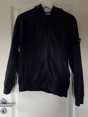 Stone Island zip hoodie  - Jättefin marinblå Stone Island zip hoodie Storlek: Junior 12 / 156 (motsvarar XS i vuxenstorlek) Passar även en vuxen som XS (jag är 160 cm och den sitter perfekt på mig). Köpt på NK i Stockholm för 2400 kr. Säljer eftersom jag inte använder den längre och den inte riktigt är min stil. 