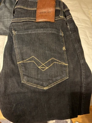 Replay Hyperflex svarta skinny jeans - Snygga svarta Replay Hyperflex jeans med skinny fit och klassisk femficksdesign. Jeansen har kontrastsömmar, bruna läderpatch med Replay-logga och coolt broderi på bakfickorna. Stretchigt material för extra komfort och stil. Skulle säga att dem är mindre i midjan, känns som 28 i midjan 