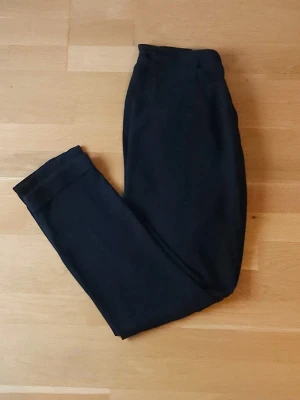 Svarta kostymbyxor - Snygga svarta kostymbyxor med hög midja och knytband i midjan. Byxorna har raka ben med uppvikta benslut och en relaxed passform. Perfekta för dig som gillar en chill och stilren look. Materialet är lätt och luftigt linne.