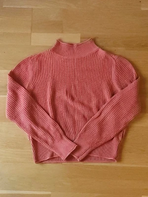 Orange tröja - Snygg stickad orange tröja med ribbade muddar och hög krage. Tröjan är perfekt för lager-på-lager under kyliga dagar. Enkel och stilren modell som är lätt att matcha.