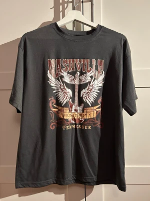 Grå t-shirt strl. XS - Grå t-shirt med vintage Nashville tryck. På lappen står det strl. XS, men den är väldigt stor i storleken, så den passar också bra på en som har strl. M.