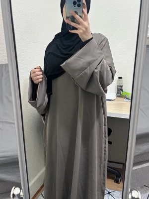 Beige lång abaya med vida ärmar - Säljer en beige långabaya  med riktigt vida ärmar och enkel, rak passform. Klänningen är helt enfärgad och har en stilren look som är lätt att matcha. Materialet känns mjukt och har ett snyggt fall. Perfekt för dig som gillar minimalistisk stil.