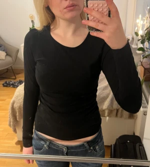 Svart långärmad topp i bomull - Säljer en enkel svart långärmad topp med rund hals. Modellen är tight och croppad, perfekt att matcha med jeans eller kjol. Materialet är mjuk bomull som sitter skönt mot kroppen. Stilren och klassisk design utan detaljer.