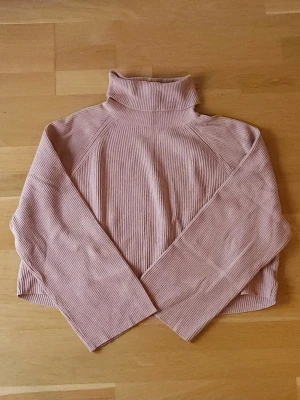 Beigerosa tröja - Supermysig beigerosa tröja med ribbad struktur och långa ärmar. Tröjan har en hög krage och är något croppad i modellen. Perfekt för lager-på-lager under kyliga dagar.