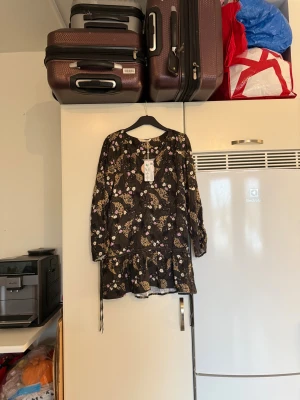 Odd Molly blommig kortklänning - Supersöt kortklänning från Odd Molly i modellen Tiffany Short Dress. Men jag tycker mer det är en tunika/ längre topp. Tunika  är brun med blommigt mönster i beige, vitt och lila, har långa ärmar och volang nertill. Perfekt för dig som gillar unika detaljer och snygg passform. Från märket Odd Molly. Storlek 1 som enligt deras storleksguide motsvarar en S. Mer en M. Helt ny med tags/ prislapp fortfarande kvar. 