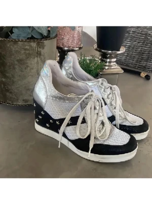 Silvriga sneakers med stjärnor och klack - Unika sneakers med silvriga och vita paneler, svart parti med små silverstjärnor och vit snörning. Skorna har en hög kilklack och holografisk detalj på hälen. Materialet är syntet och skinn, med platt sula framtill och klack baktill. Perfekt för dig som gillar att sticka ut. Perfekt till fest jul/nyår💕