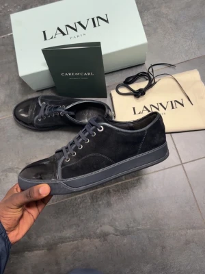 Lanvins  - Snygga svarta sneakers från Lanvin med ovandel i mjuk mocka och lackad tå. Skorna har rund tå, platt sula och klassisk snörning med metallöglor. Perfekt för dig som gillar stilrena och exklusiva sneakers med lyxig känsla.