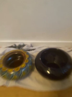 2st stora skålar av olika modeller - Bilderna visar två runda keramikvaser, en med färgglatt mönster i blått och gult och en enfärgad mörk vas. 
