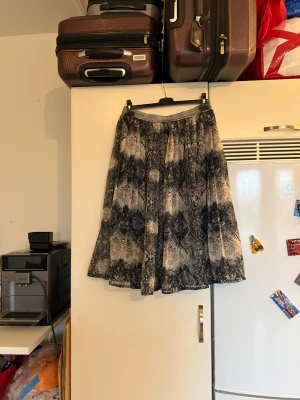 Mönstrad långkjol från Cream, stl 38 - Säljer en snygg långkjol från Cream i storlek 38. Kjolen har ett coolt ormmönster i svart, grått och beige med ett glansigt, randigt resårband i midjan. Materialet är lätt och luftigt, perfekt för dig som gillar statement-plagg med flow. Mycket fint skick, jag hittar inga synliga anmärkningar eller defekter. 