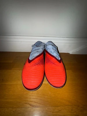 Nike Phantom GT2 elite - Nike Phantom GT2 fotbollsskor med en snygg mix av rött och ljusblått. Skorna har snörning, platt sula med dobbar och är tillverkade i syntetmaterial för grym känsla på planen. Svarta Nike-loggor och coola detaljer längs sidorna. Perfekt för dig som vill sticka ut på matchen.