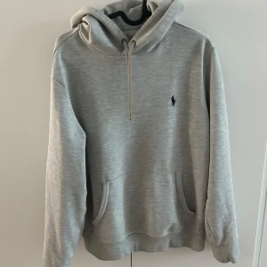 Grå hoodie från Ralph Lauren - Säljer en stilren grå hoodie från Ralph Lauren med en klassisk känguruficka och justerbar huva. Den har en liten broderad logga på bröstet. Perfekt för en avslappnad look. Storleken är S