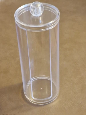 Genomskinlig behållare för bomullsrondeller - Snygg och praktisk cylindrisk hållare i transparent plast med lock och rund knopp. Någon repa och mindre märke i plasten men det var svårt att få med på bild. Ca 19 cm hög med locket på.