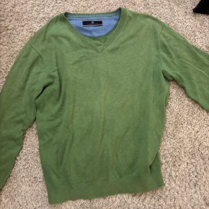 Grön v-ringad tröja Hansen & Jacob - Snygg grön v-ringad tröja från Hansen & Jacob i mjuk bomull. Tröjan har ribbade muddar vid ärmslut och nederkant samt långärmad passform. Perfekt för dig som gillar stilrena och klassiska plagg med lite färg.