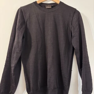 Mörkblå merinoull stickad tröja Oscar Jacobson - Snygg mörkblå stickad tröja från Oscar Jacobson i storlek S. Klassisk rund halsringning och ribbade muddar vid ärmslut och nederkant. Perfekt för dig som gillar stilrena och tidlösa plagg med skön passform.