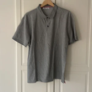 Grå pikétröja från Calvin Klein - Snygg grå pikétröja från Calvin Klein Golf i klassisk modell med krage och knappar framtill. Tröjan har diskret 'ck'-brodyr på bröstet och är tillverkad i mjuk bomull. Perfekt för en clean och stilren look.